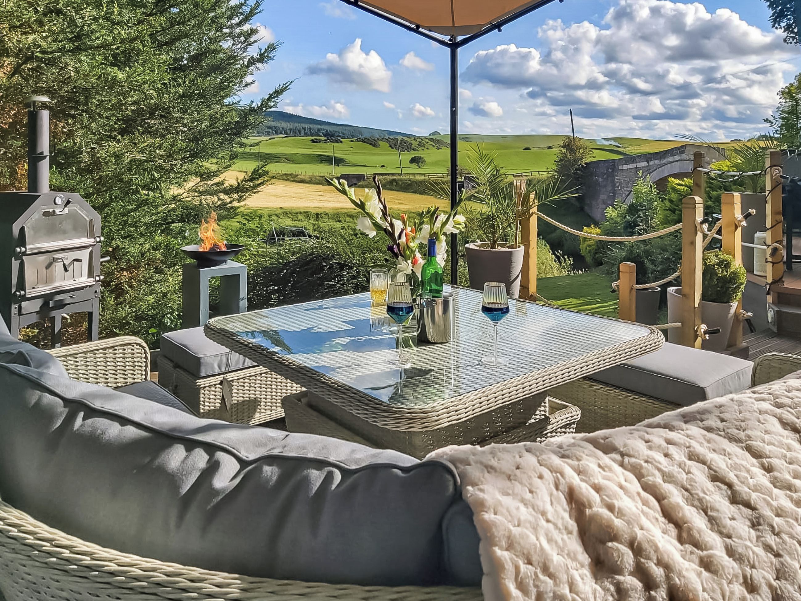 Une terrasse extérieure aménagée avec des meubles en osier, une table en verre et un barbecue.