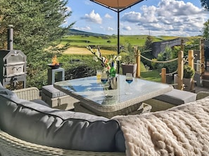 Une terrasse extérieure aménagée avec des meubles en osier, une table en verre et un barbecue.