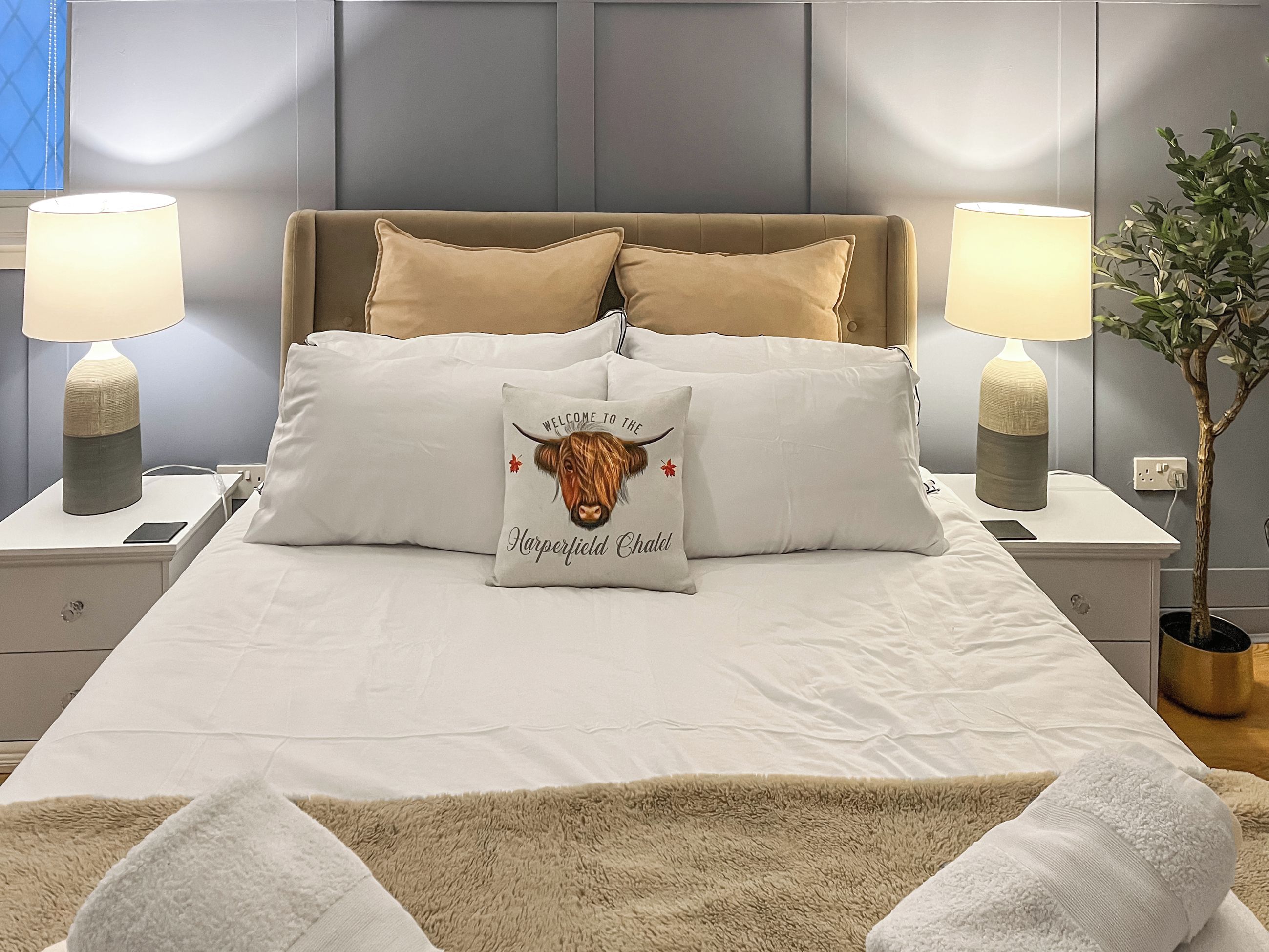 Un lit bien fait, agrémenté d’un coussin décoratif, de lampes de chevet et d’une plante.