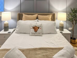 Un lit bien fait, agrémenté d’un coussin décoratif, de lampes de chevet et d’une plante.