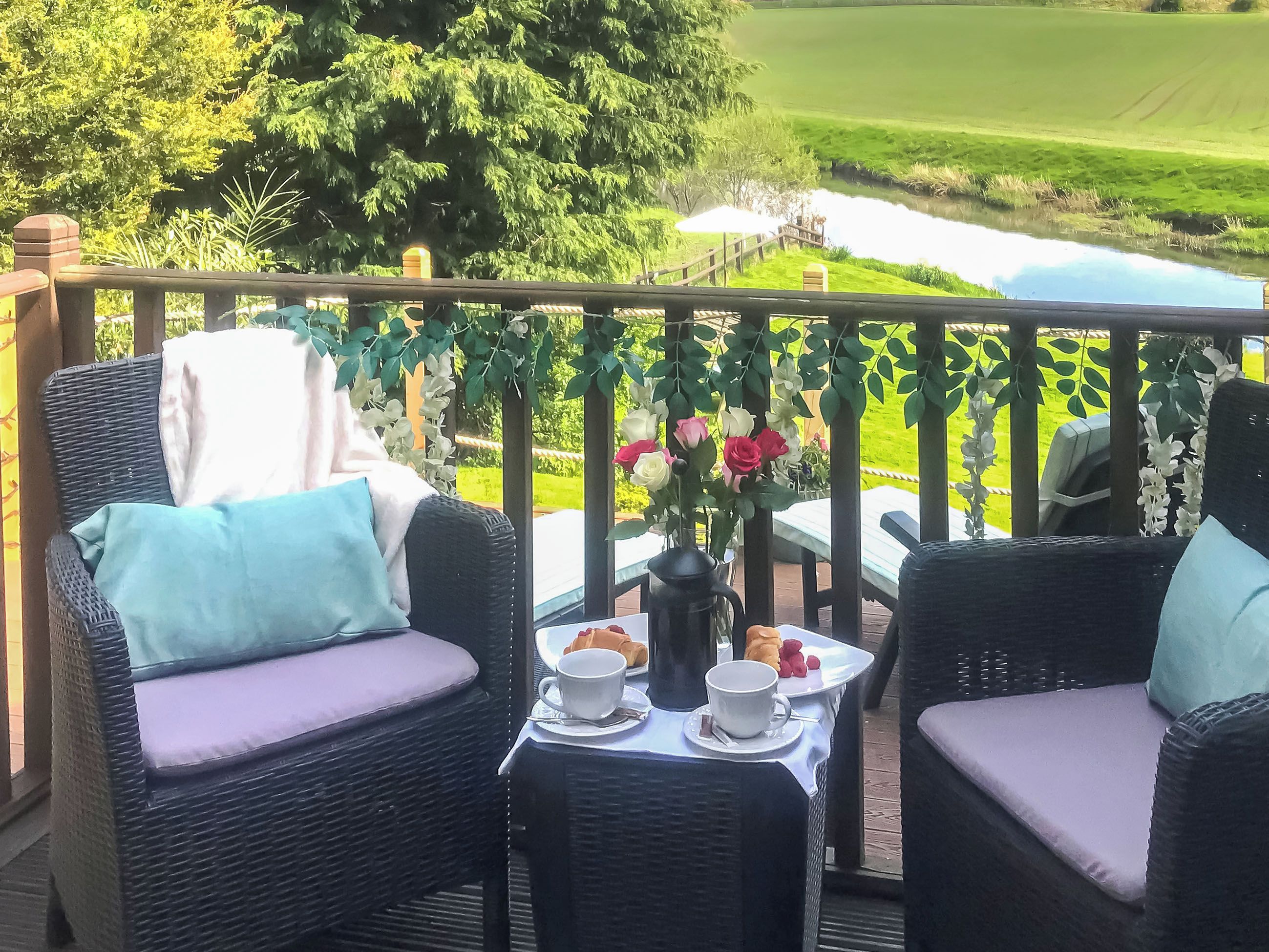 Un balcon avec des fauteuils en osier, une table ornée d’un vase de fleurs et une vue sur un terrain de golf.