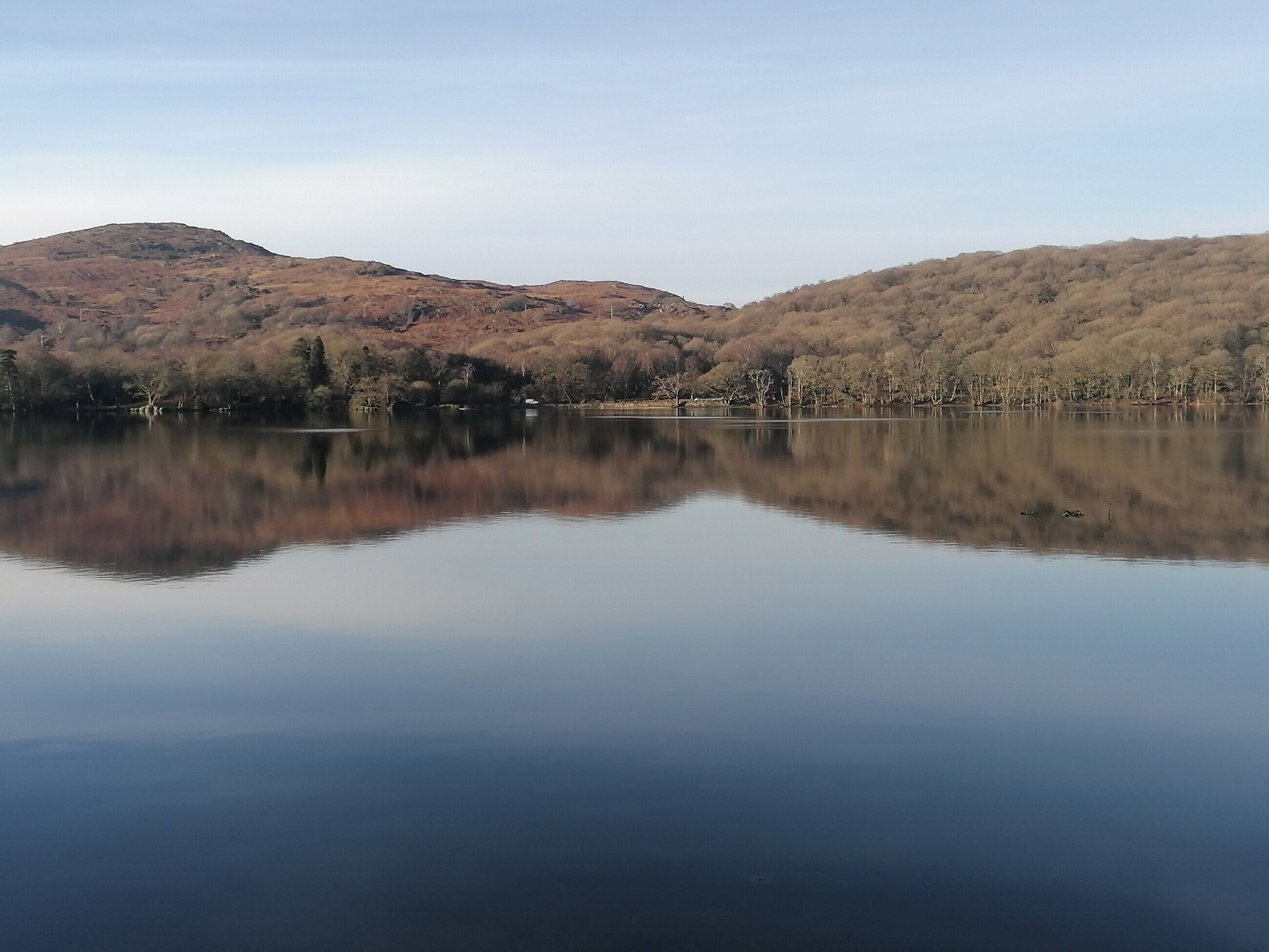 A calm lake with a clear reflection of the surrounding hills and sparse trees.
