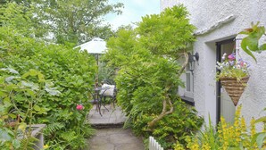 A narrow garden path leading to a white building with a window and a hanging flower basket. - 1 bedroom accommodation in Bouth, Newby Bridge (Bouth, Newby Bridge)