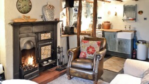 A cozy living room with a fireplace, leather armchair, and a dining area with wooden beams. - 1 bedroom accommodation in Bouth, Newby Bridge (Bouth, Newby Bridge)