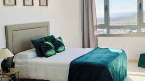 Quarto com cama, mesa de cabeceira, abajur e janela com vista para a paisagem.