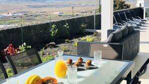 Mesa com itens de café da manhã, vista para o campo e área externa com mesas.