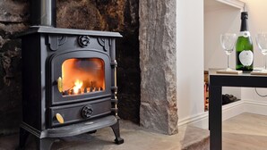 A stone fireplace with a black wood-burning stove, a bottle of wine, and two glasses on a table. - 3 bedroom accommodation in Gartocharn, near Drymen (Gartocharn, near Drymen)
