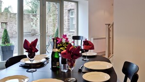 A dining table set with plates, wine glasses, and a bottle of wine, with a pendant light above and a view of a stone building outside. - 3 bedroom accommodation in Gartocharn, near Drymen (Gartocharn, near Drymen)