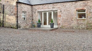 A stone building with a gravel driveway, a large sliding glass door, and two potted plants. - 3 bedroom accommodation in Gartocharn, near Drymen (Gartocharn, near Drymen)