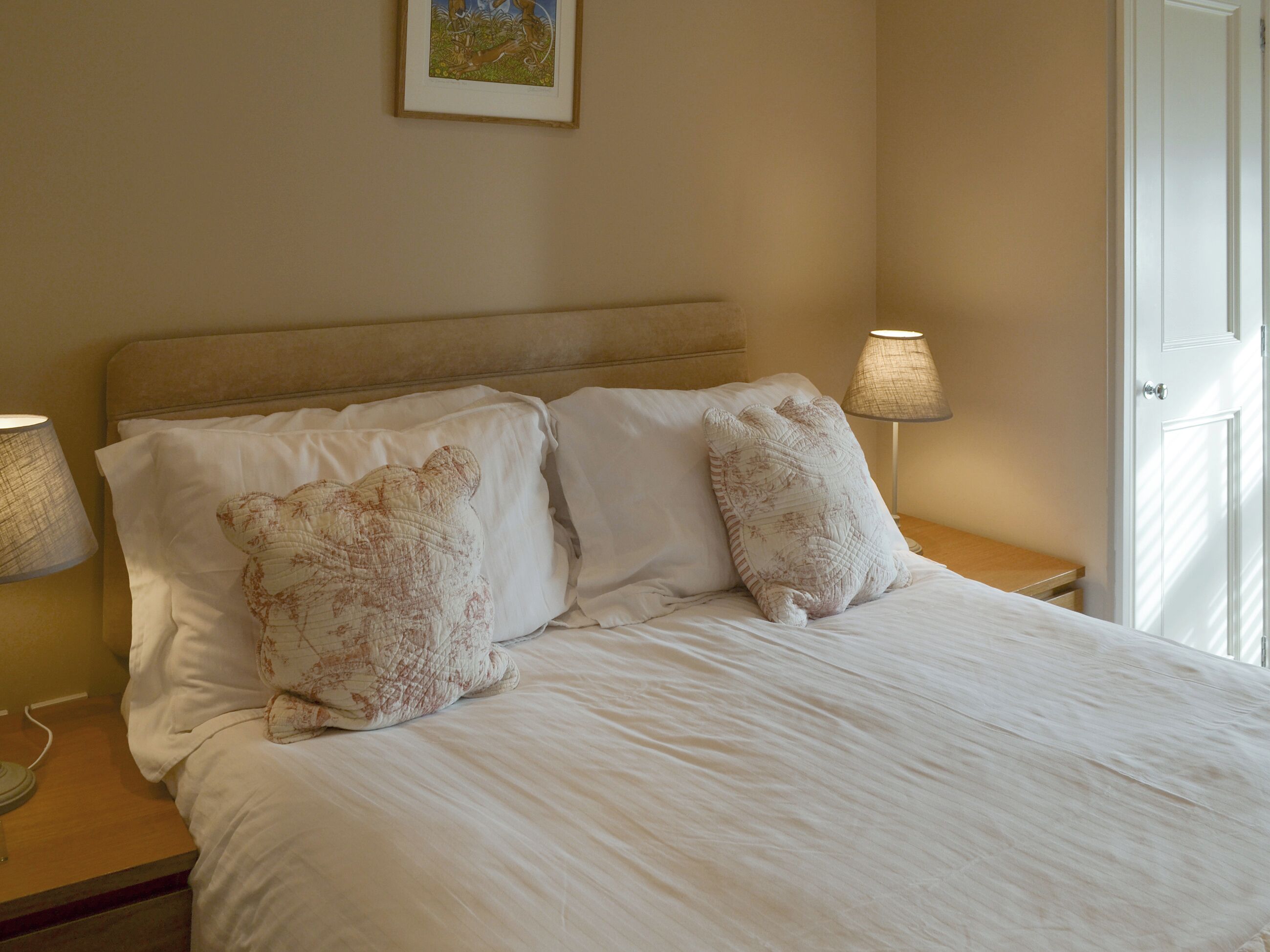 Een netjes opgemaakt bed met twee kussens, een bedlampje en een ingelijst foto aan de muur.