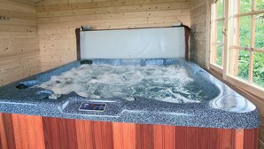 Un bain à remous doté d’un panneau de commande, de parois en bois et d’une fenêtre donnant sur un paysage verdoyant.