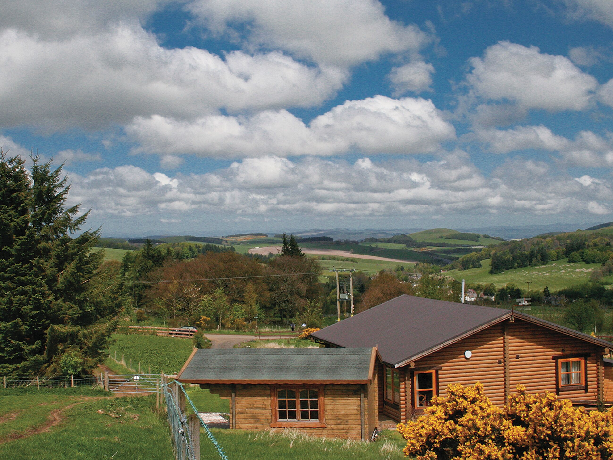 A log cabin with a sloped roof, surrounded by lush greenery and a clear sky.