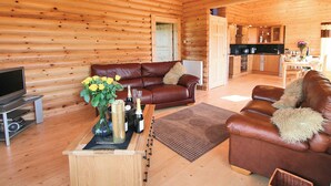 L’intérieur d’une cabane en rondins présente un salon avec un canapé en cuir marron, une table basse agrémentée d’objets décoratifs et un téléviseur.