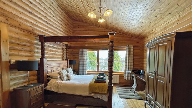 Une chambre dans un chalet en rondins, avec un lit à baldaquin, des murs en bois, une grande fenêtre et une armoire.