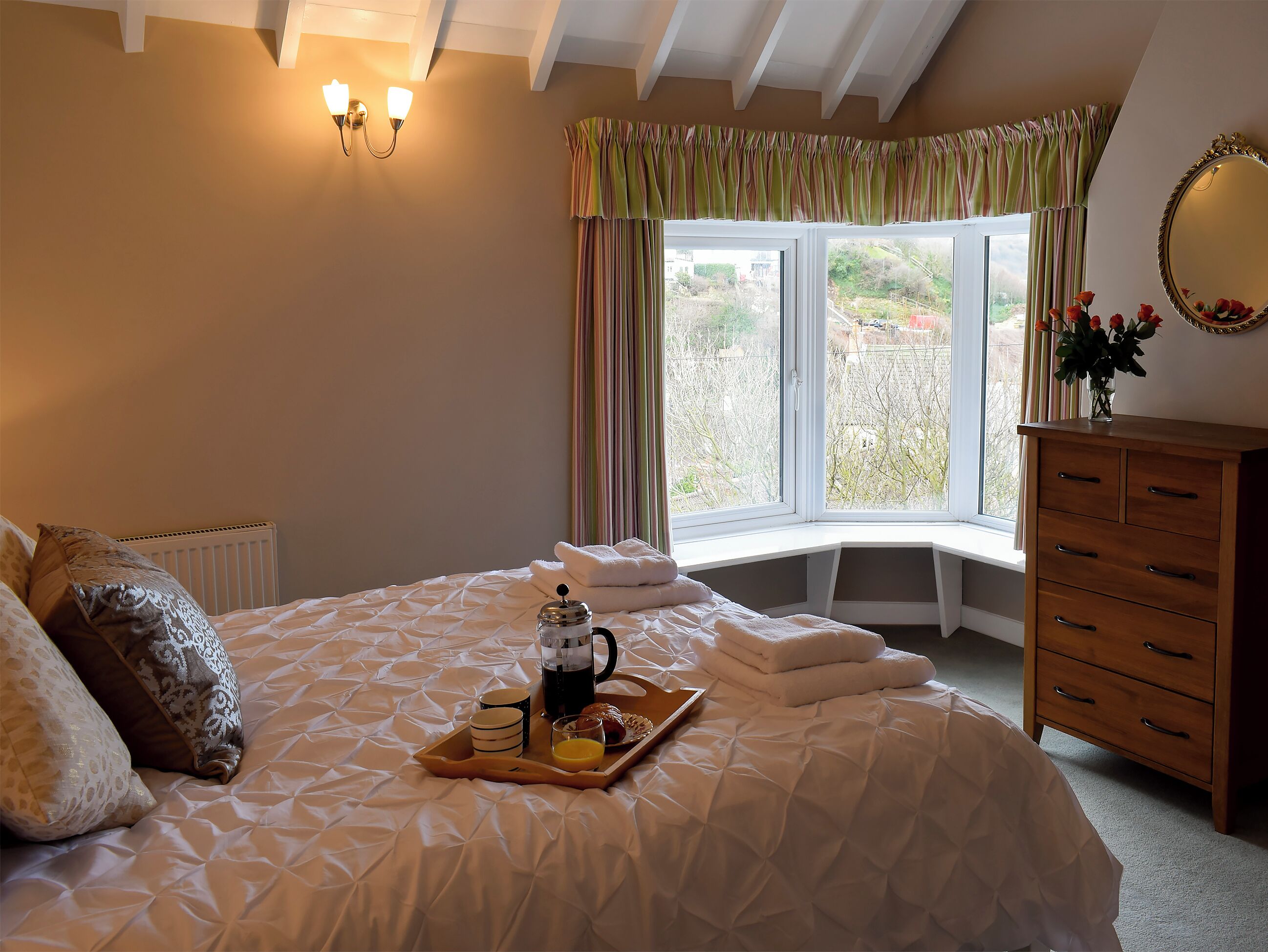 Une chambre à coucher avec un grand lit, une commode en bois, une fenêtre avec des rideaux et un radiateur.