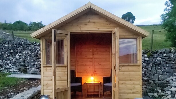 A small wooden cabin with an open door, a single chair inside, and two metal containers outside. - 2 bedroom accommodation in Ravenstonedale, near Kirkby Stephen (Ravenstonedale, near Kirkby Stephen)
