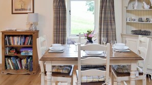 A dining area with a wooden table set for four, surrounded by white chairs with plaid cushions. A bookshelf filled with books is to the left. - 2 bedroom accommodation in Ravenstonedale, near Kirkby Stephen (Ravenstonedale, near Kirkby Stephen)
