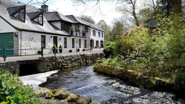 A white building with a stone bridge over a river, surrounded by greenery and trees. - 1 bedroom accommodation in Dalbeattie, near Dumfries (Dalbeattie, near Dumfries)