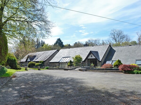 A row of stone buildings with pitched roofs, a gravel driveway, and surrounding greenery.