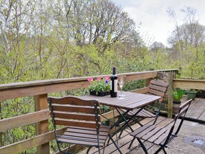 Een houten terras met een tafel en banken, omringd door groen.