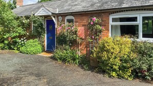 A brick house with a blue door, a small porch, and a garden with various plants and flowers. - Looking for a romantic escape in Herefordshire’s rolling countryside. (Tarrington, near Ledbury)