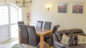 Un comedor con mesa de madera y seis sillas, un sofá de cuero con cojines estampados y dos lámparas de pared.