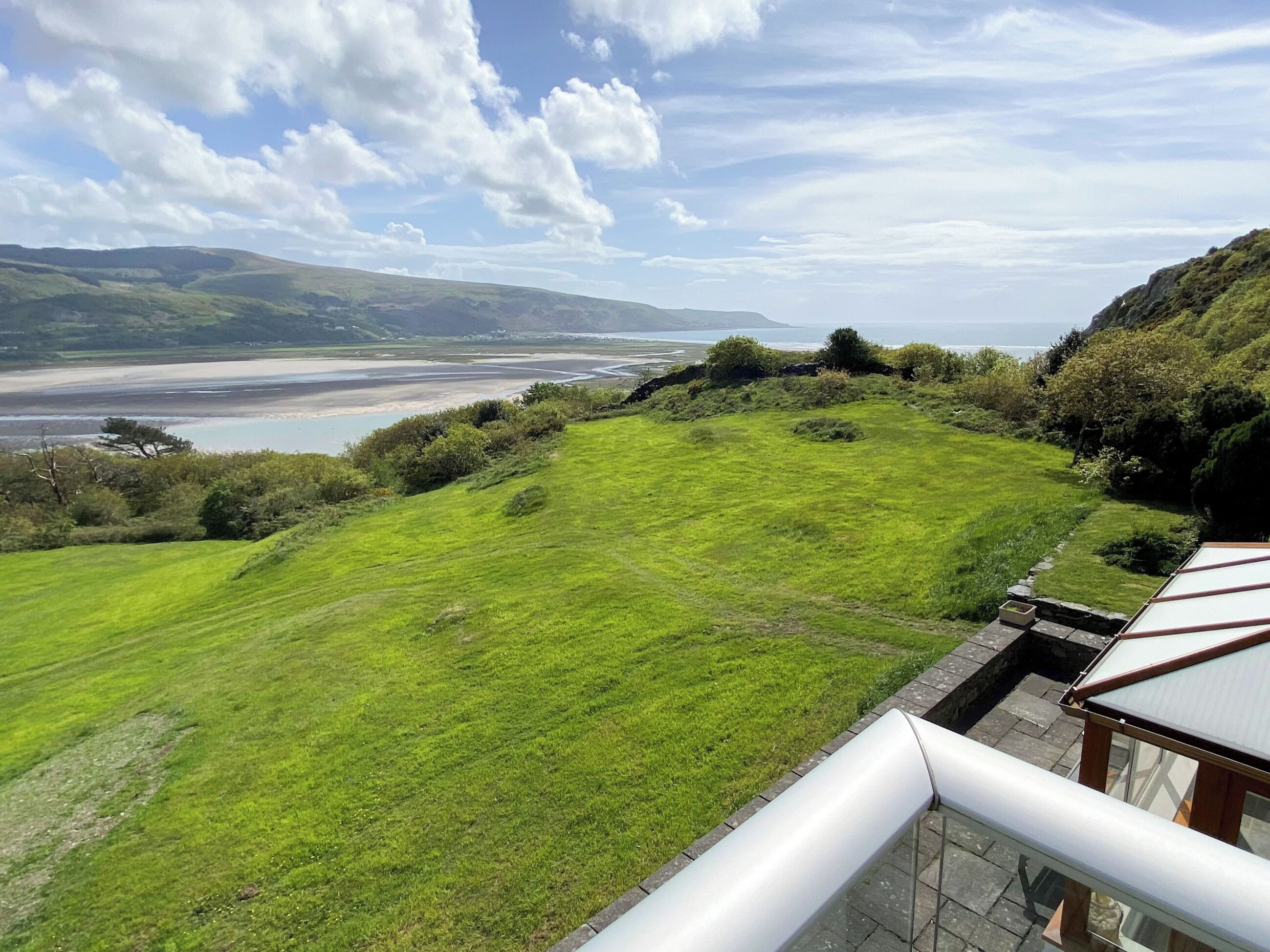 A grassy field with a view of a beach and mountains in the distance.