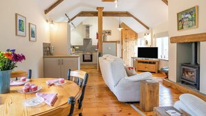 Een gezellige woonkamer met een open haard, houten balken, een eethoek met een gedekte tafel en een keuken op de achtergrond.
