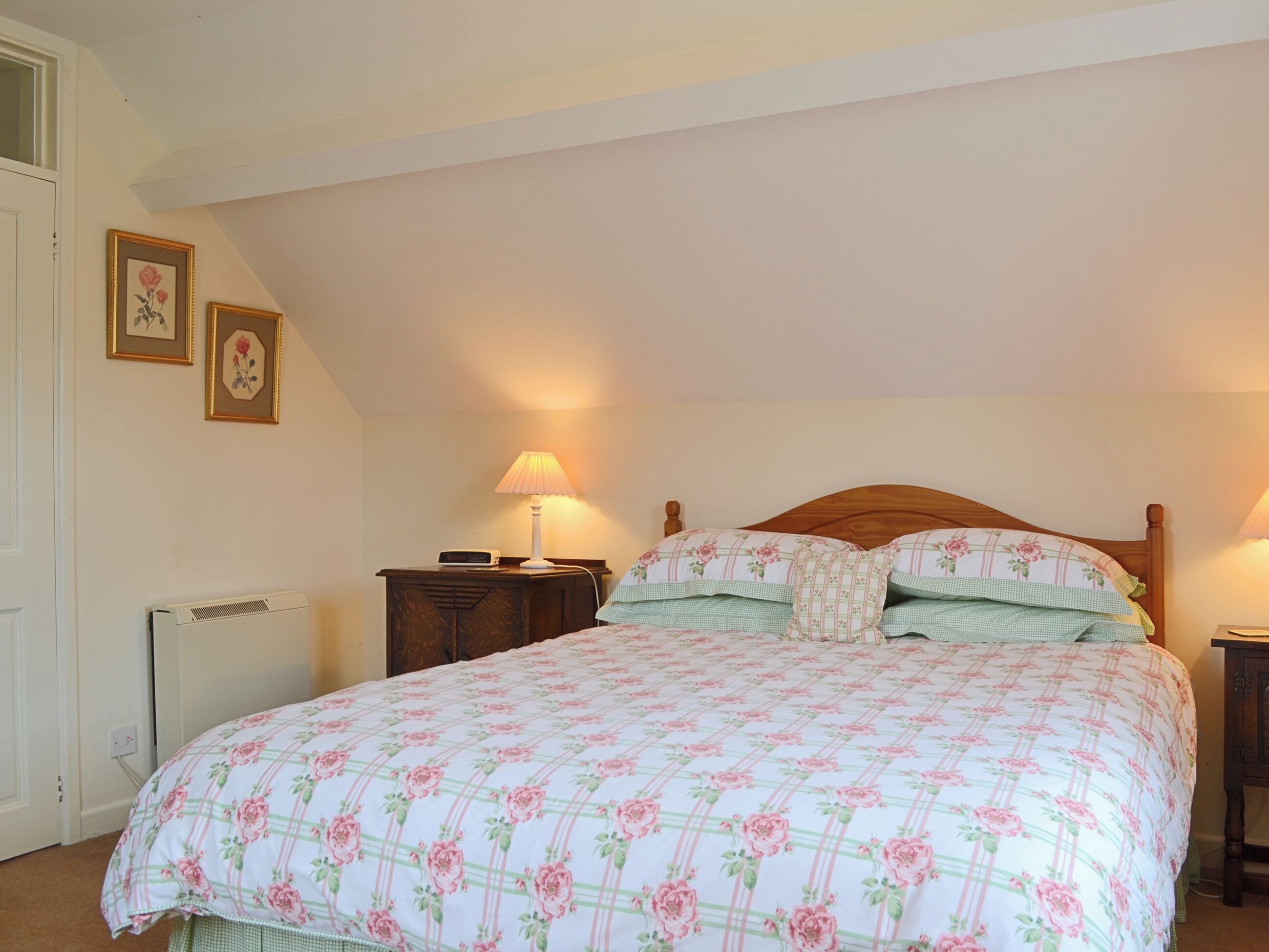 A bedroom with a floral-patterned bedspread, a wooden headboard, two bedside lamps, and a nightstand with a lamp.