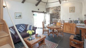 Una sala de estar acogedora con un sofá, una mesita de centro y un comedor con sillas. Hay una cocina con pared de piedra y electrodomésticos modernos.