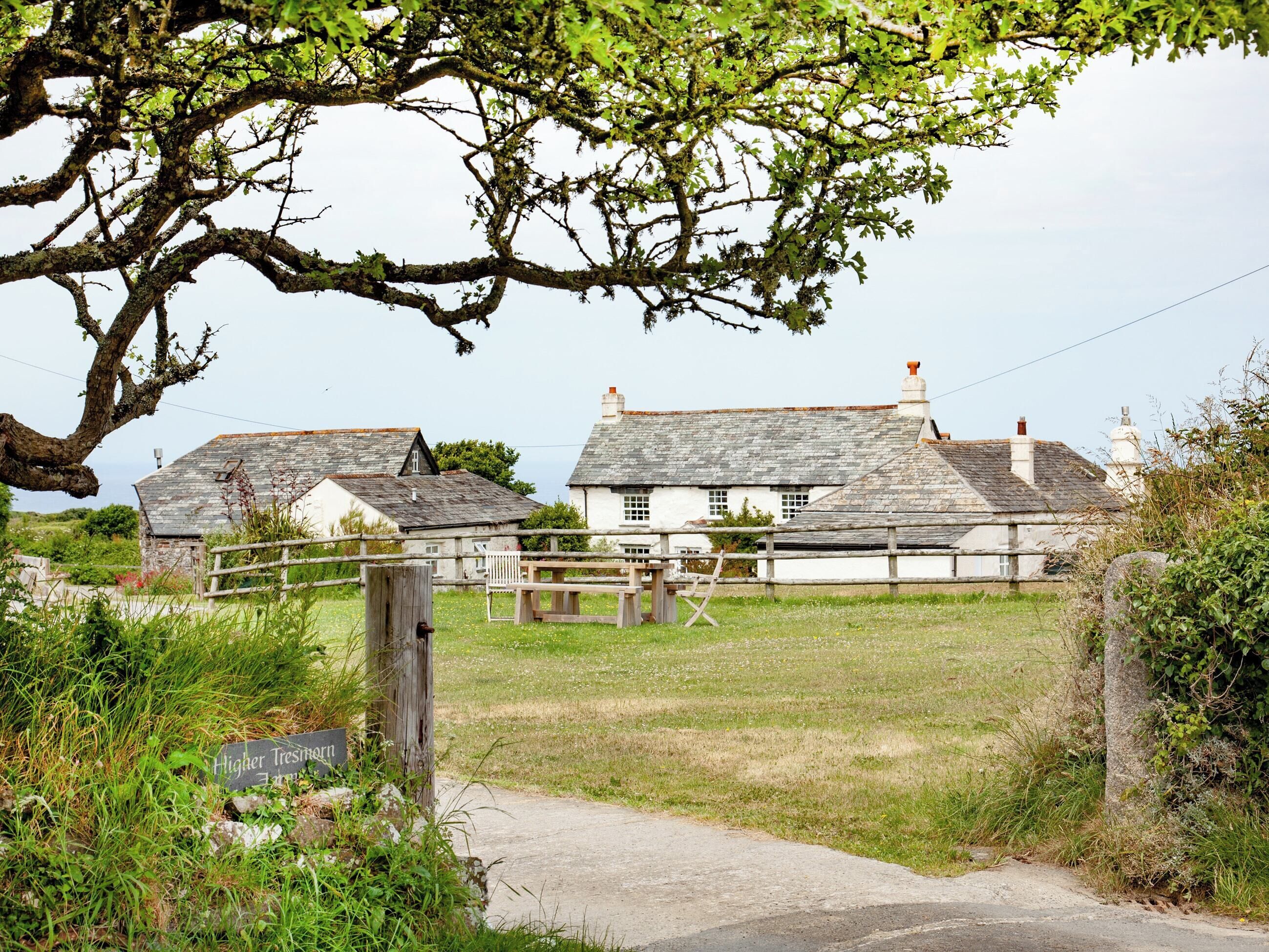 Un cadre rural avec des maisons traditionnelles en pierre, une clôture en bois et un panneau indiquant « Higher Treshern Farm ».