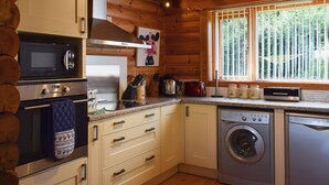 A compact kitchen with a microwave, stove, oven, and dishwasher. There is a window with a view of trees. - Fingask Log Cabin - S4394 (Glenfarg)