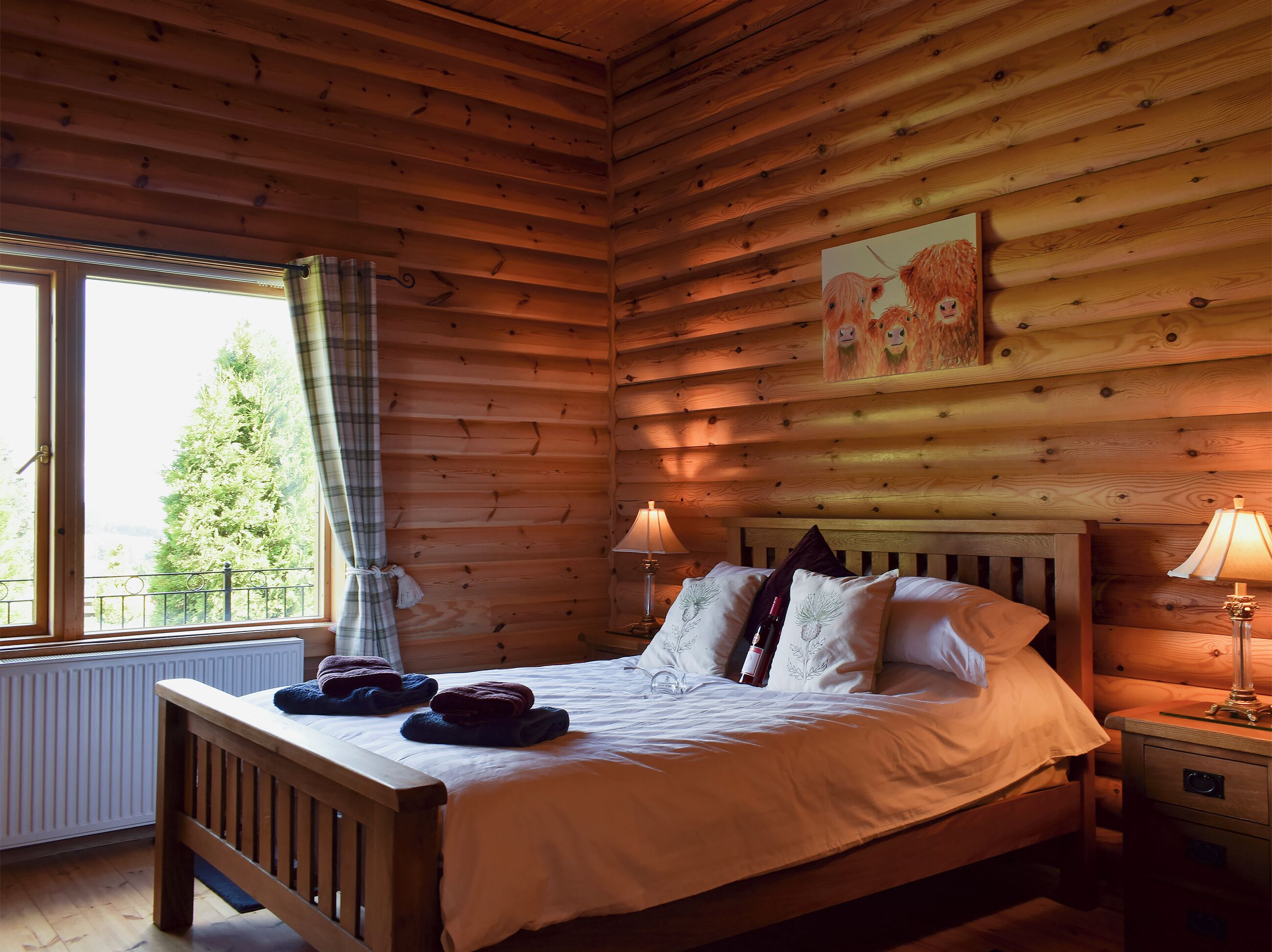 Ein Schlafzimmer einer Holzhütte mit einem Bett, zwei Nachttischlampen, einem Fenster mit Vorhängen und einer Heizung.