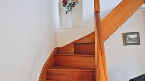 Un escalier en bois mène à un palier où se trouve un tableau encadré et une petite fenêtre agrémentée d’un arrangement floral.
