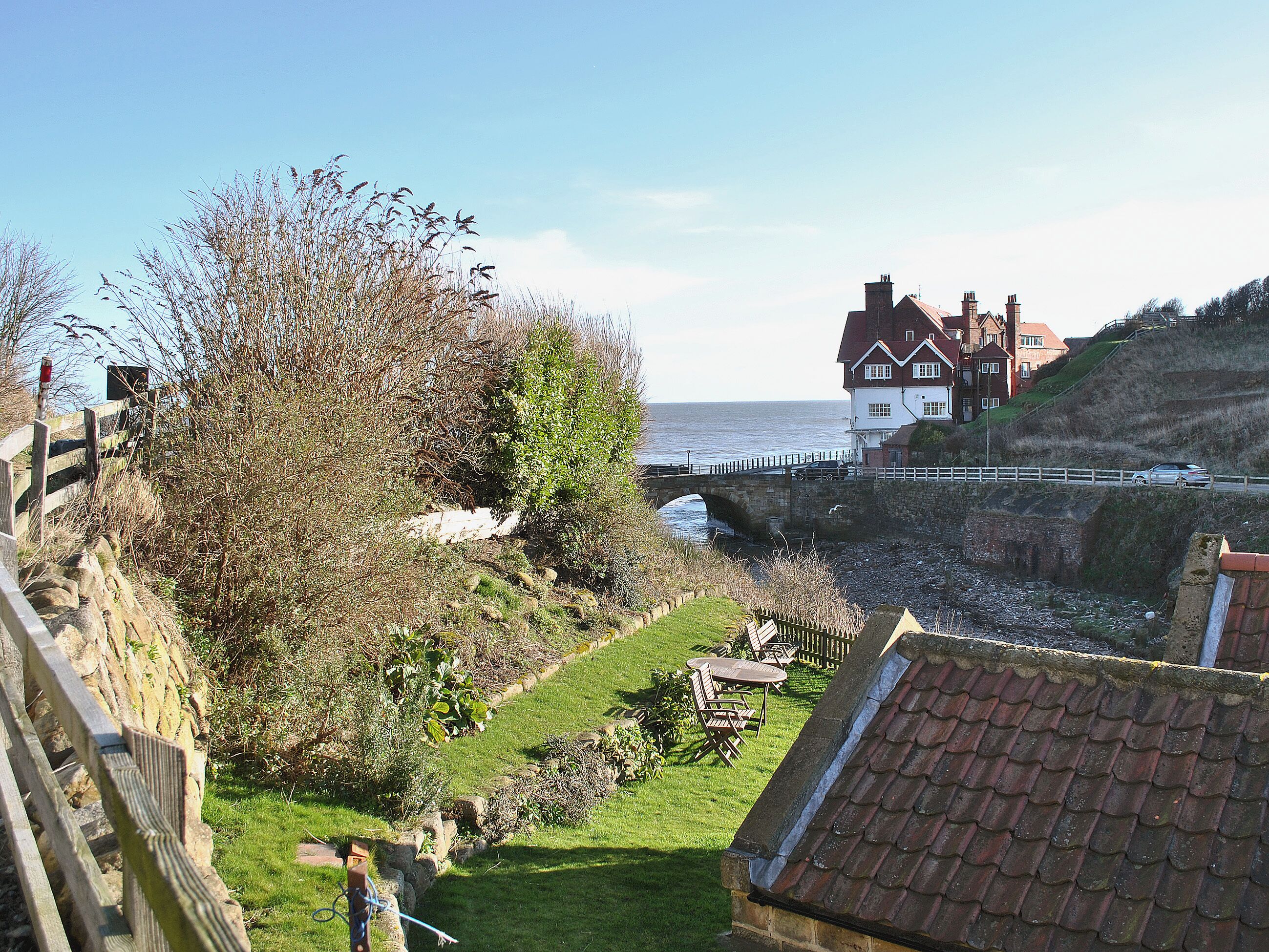 A coastal view with a stone bridge, grassy areas, and a building with a red roof.