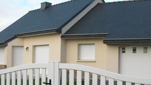 A residential building with a dark roof, beige walls, and white garage doors. - PENVENAN 22710. House 4 PERSONS. Close to shops. 3km from beaches (Penvénan)