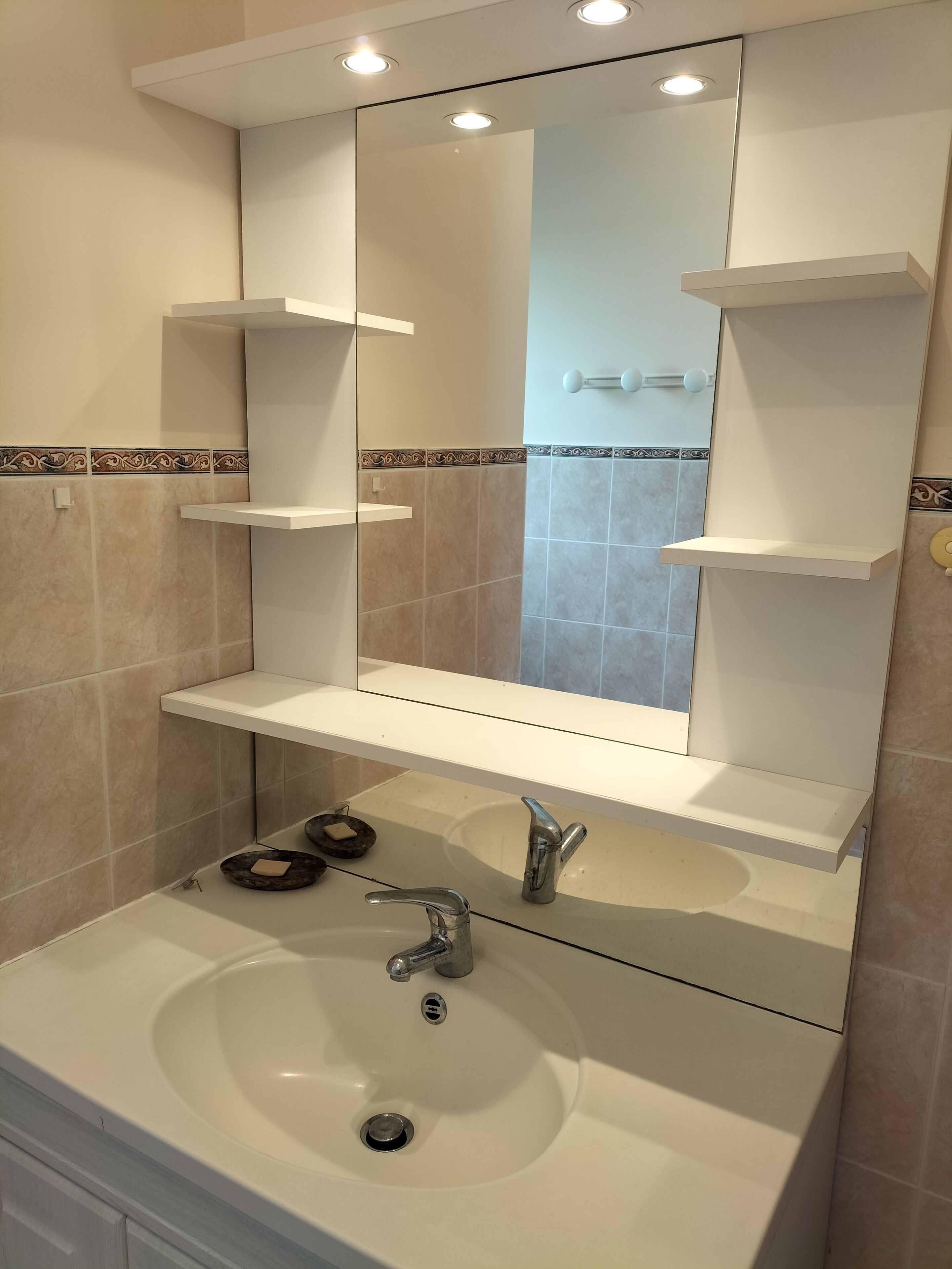 A bathroom with a white sink, a mirror, and two white shelves above it.