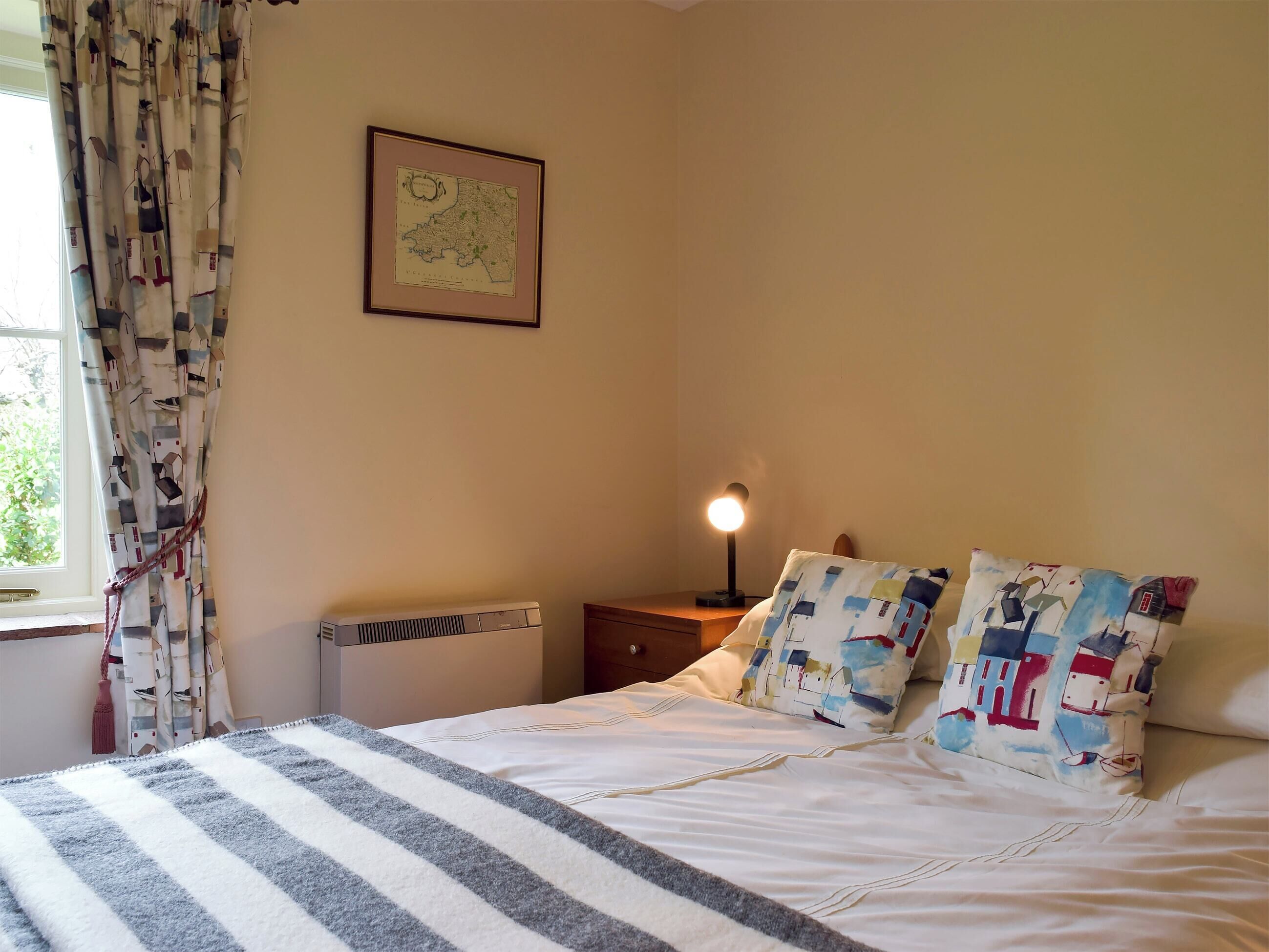 A bedroom with a bed, a nightstand, a lamp, a radiator, and a map on the wall.