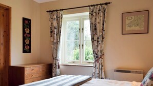 A bedroom with a bed, a window with curtains, a dresser, and a map on the wall.
