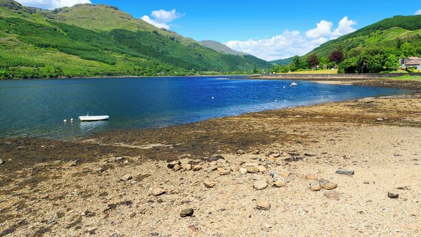A lake with a boat, rocky shore, and green hills in the background. - 2 bedroom accommodation in Ardentinny, near Dunoon (Ardentinny, near Dunoon)