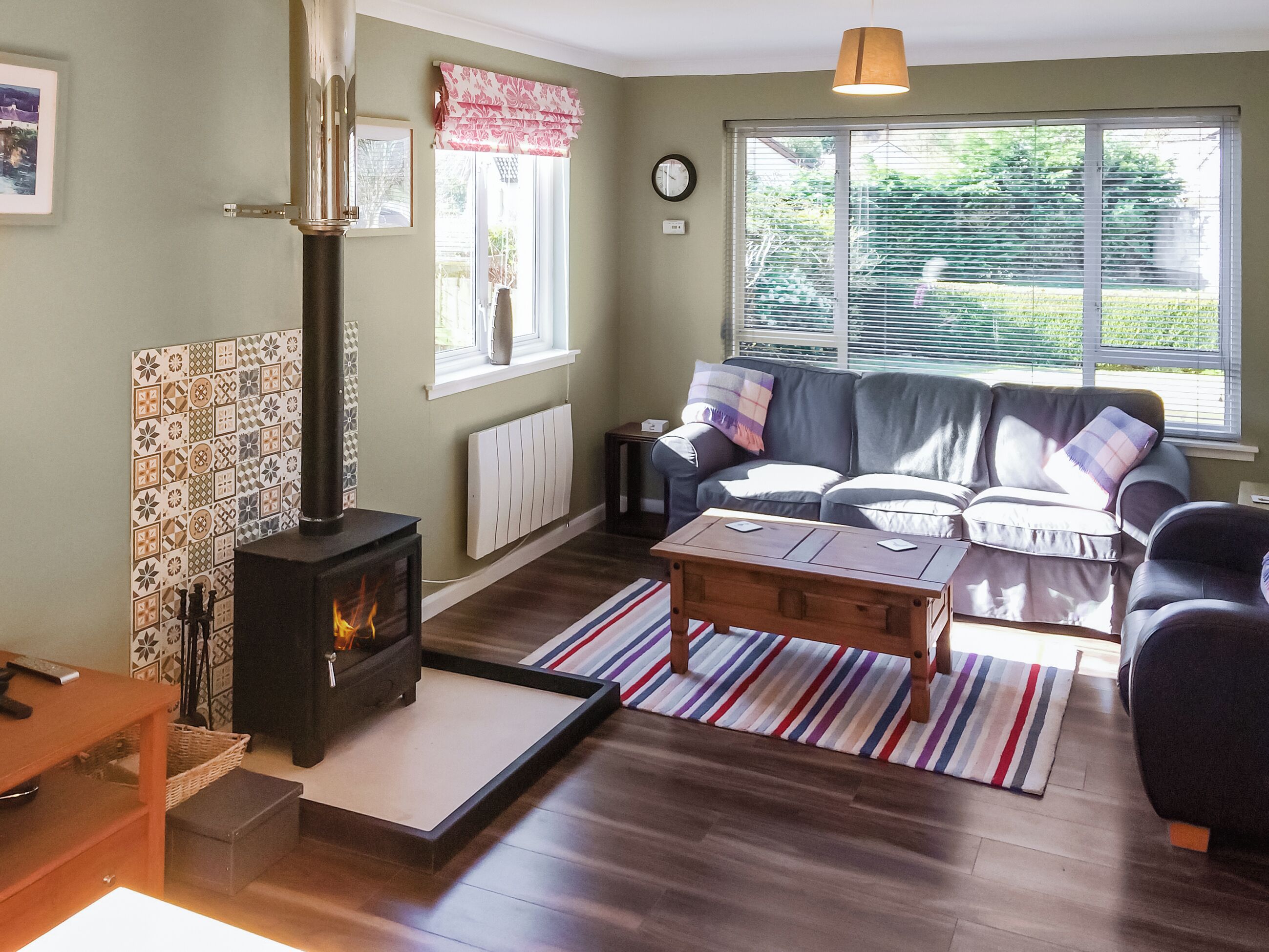 A cozy living room with a wood-burning stove, a sofa, a coffee table, and a view of greenery outside.