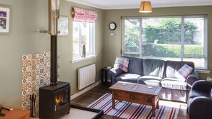 A cozy living room with a wood-burning stove, a sofa, a coffee table, and a view of greenery outside. - 2 bedroom accommodation in Ardentinny, near Dunoon (Ardentinny, near Dunoon)