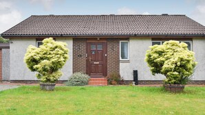 A two-story house with a brown door, a brick wall, and a tiled roof. There are two potted plants in front of the house. - 2 bedroom accommodation in Ardentinny, near Dunoon (Ardentinny, near Dunoon)