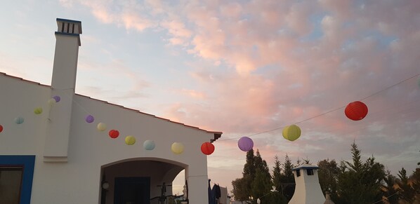 A building with a white facade, a chimney, and a series of colorful paper lanterns strung across the front. - Villa with pool in the Ourique region <br>sleeps 9 4 bedrooms (ALDEIA NOVA FAVELA)