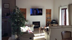 Ein Wohnzimmer mit an der Wand befestigtem Fernseher, einer Couch, einem Couchtisch und einem Bücherregal.