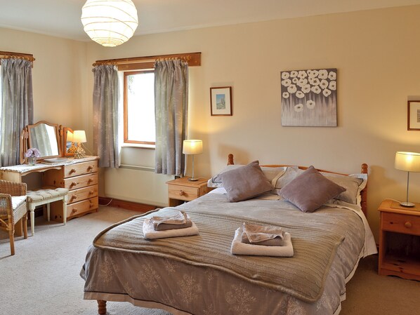 Une chambre à coucher comprenant un lit, des tables de chevet, une commode, un bureau et une fenêtre avec des rideaux.