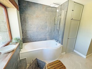 Een badkamer met een badkuip, douche en een raam met een plant.