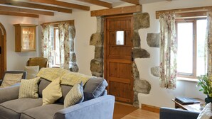 Una sala de estar acogedora con un sofá, sillas, una puerta de madera, paredes de piedra y una ventana con cortinas florales.