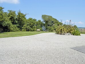 Un chemin de gravier mène à un banc situé dans un espace aménagé, agrémenté d’arbres et offrant une vue sur un ciel dégagé.