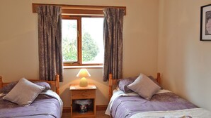 Un dormitorio con dos camas, una mesita de noche con lámpara, una ventana con cortinas y un cuadro enmarcado en la pared.